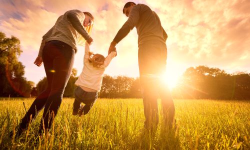 Happy family in the park evening light. The lights of a sun. Mom, dad and baby happy walk at sunset. The concept of a happy family.Parents hold the baby's hands.