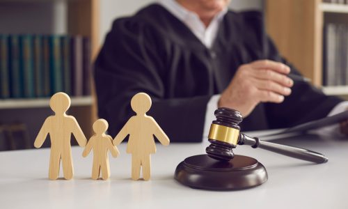 Gavel, sound block and small wooden figurines of husband, wife and kid on judge's table in courthouse during court hearing. Family law, divorce lawyer, joint custody of child and alimony concept